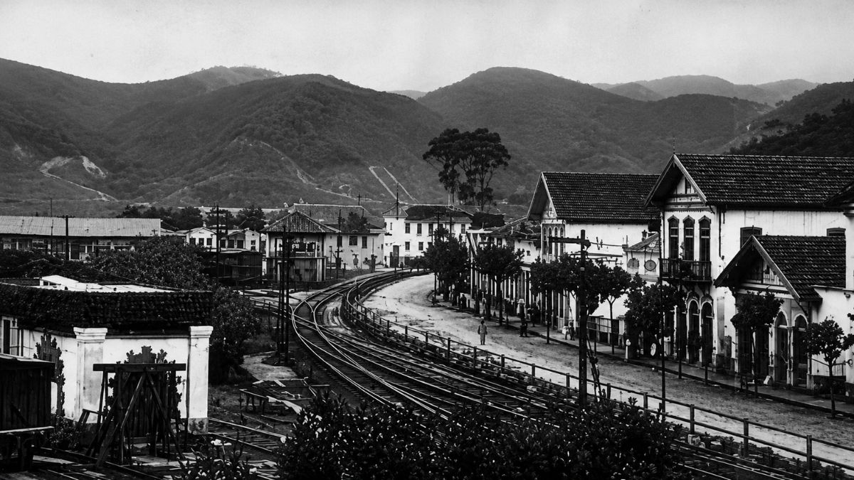 Fotografia antiga em preto e branco mostrando entroncamento ferroviário entre casarios e montanhas.
