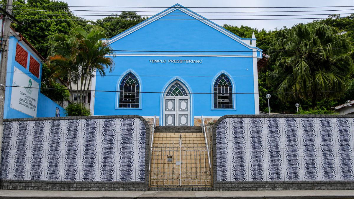 Fotografia da fachada de um templo religioso azul com detalhes brancos. O edifício possui janelas e porta em arco ogival. À frente existe um muro com azulejos decorativos e uma escadaria central.