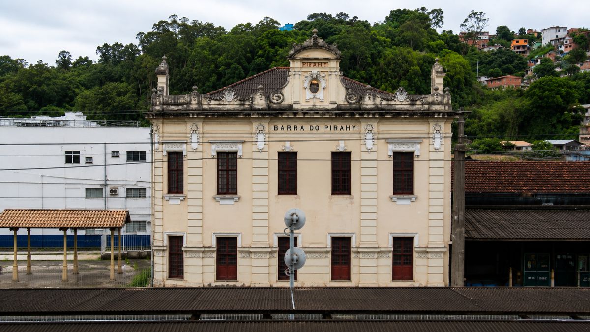 Fachada frontal de prédio histórico neoclássico com a inscrição Barra do Pirahy sob frontão decorado e morro verde ao fundo.