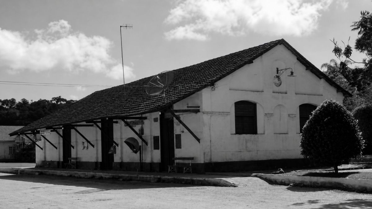 Fotografia em preto e branco de uma estação ferroviária antiga com telhado extenso.