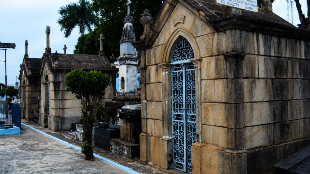 Fotografia de túmulos antigos construídos em blocos de pedra apresentando portões de ferro azul trabalhados e ornamentos em estilo clássico.