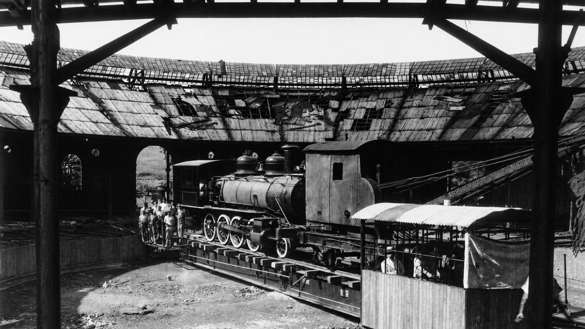 Fotografia em preto e branco do interior de uma oficina ferroviária circular com locomotiva.