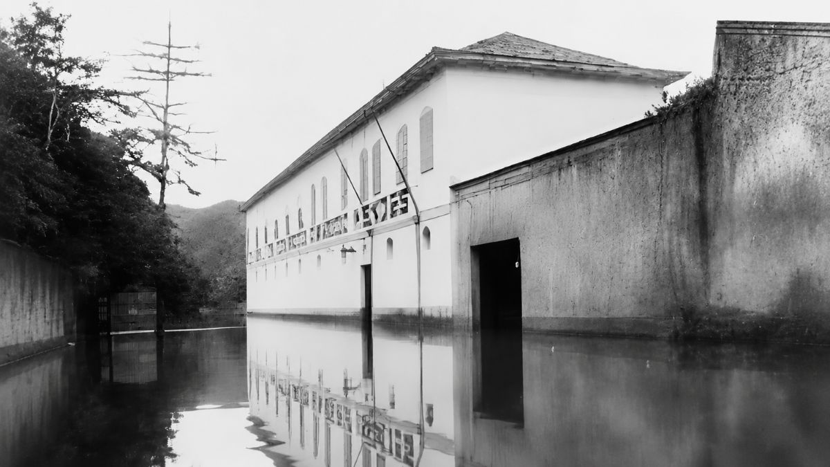 Fotografia em preto e branco de um casarão histórico com a base submersa pela enchente.