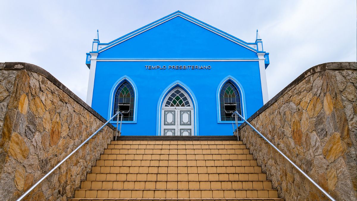 Vista frontal centralizada de uma igreja azul a partir de uma escadaria de cerâmica clara flanqueada por muros de pedra. O edifício possui porta e janelas em arco ogival.