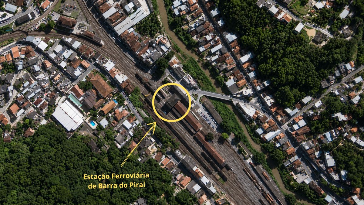Fotografia aérea de drone mostrando a malha ferroviária, o Rio Piraí e o centro urbano com marcação na estação.