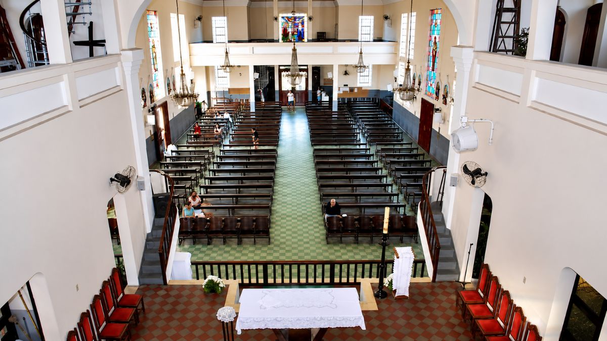 Fotografia do alto mostrando a nave única com bancos de madeira, vitrais laterais, altar ao fundo e coro no mezanino.