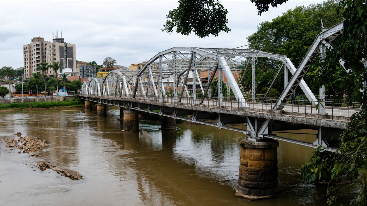 Fotografia colorida da Ponte Getúlio Vargas com cinco arcos metálicos brancos sobre o Rio Paraíba do Sul e prédios ao fundo.