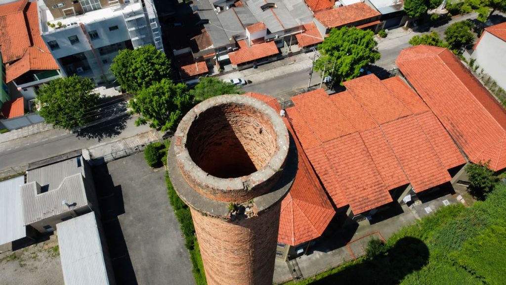 Foto aérea aproximada do topo circular da chaminé de tijolos mostrando sua abertura interna e o entorno urbano residencial.