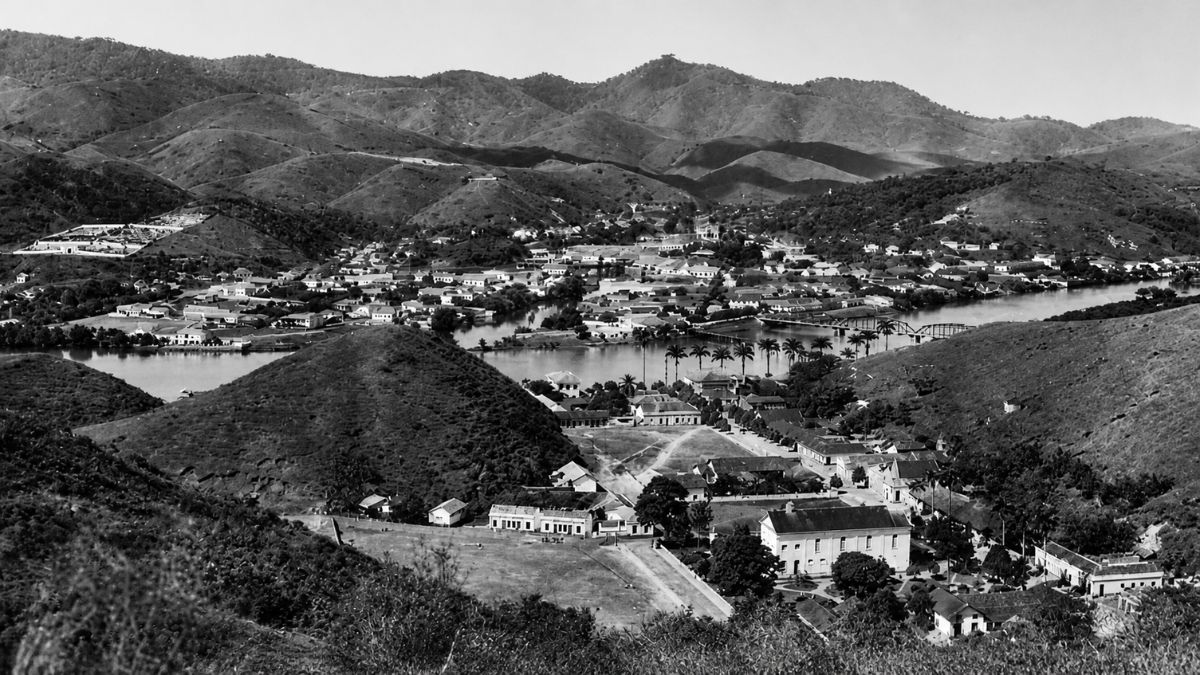 Fotografia aérea antiga em preto e branco revelando a cidade entre morros e rios.