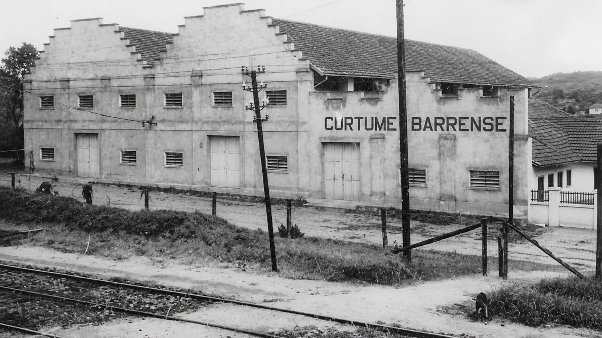 Fotografia em preto e branco de um grande galpão industrial com o nome escrito.