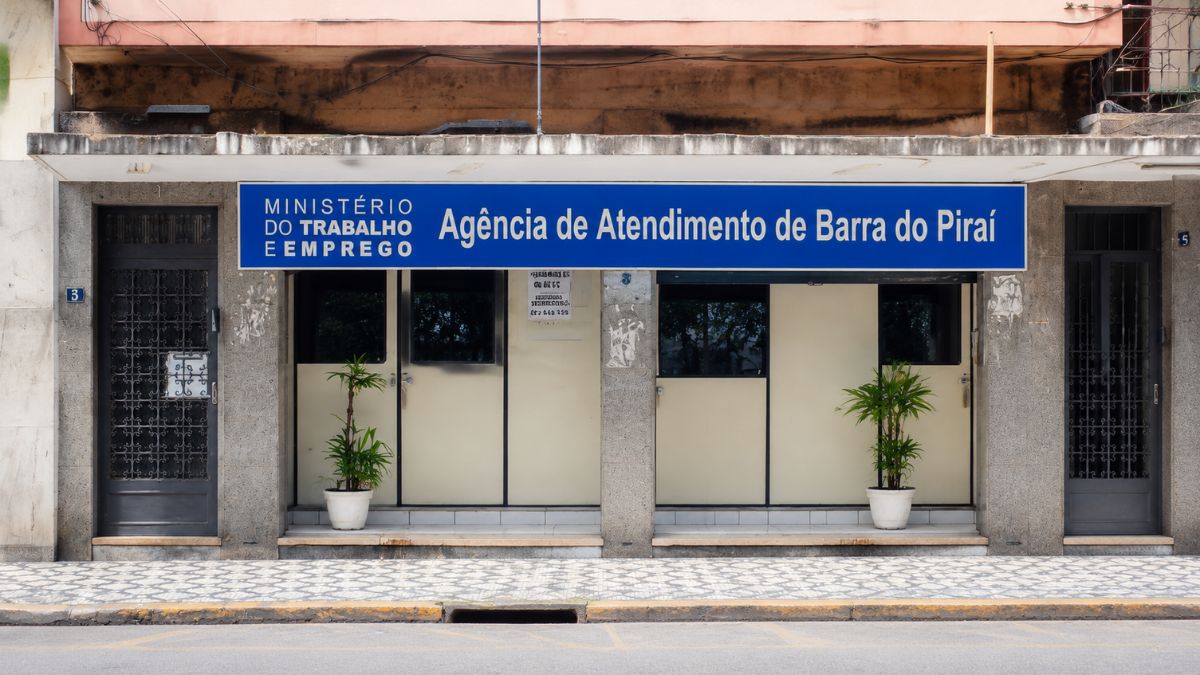 Fotografia da fachada da Agência de Atendimento de Barra do Piraí do Ministério do Trabalho e Emprego destacando a entrada com portas escuras, vasos de plantas e uma grande placa informativa azul.