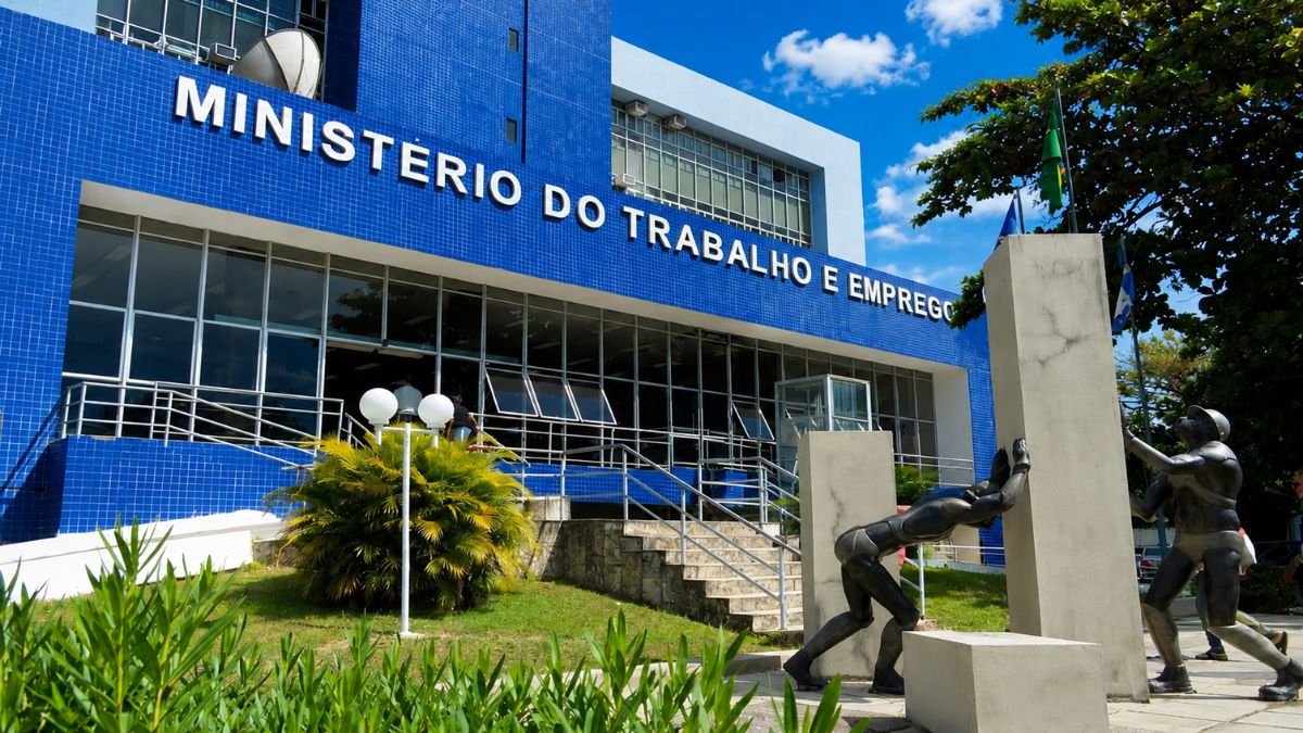 Fachada de prédio azul com letreiro branco do Ministério do Trabalho e Emprego, escada de acesso e estátuas pretas na frente.
